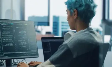 Application programmer seated in front of dual monitors in office environment coding